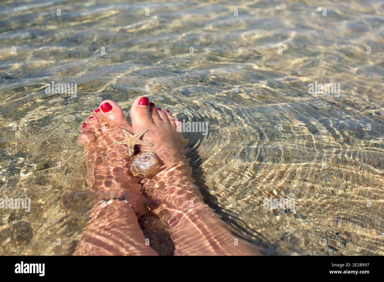 Frauenfüße mit Pediküre, die unter dem Wasser am Strand liegen Stockfoto