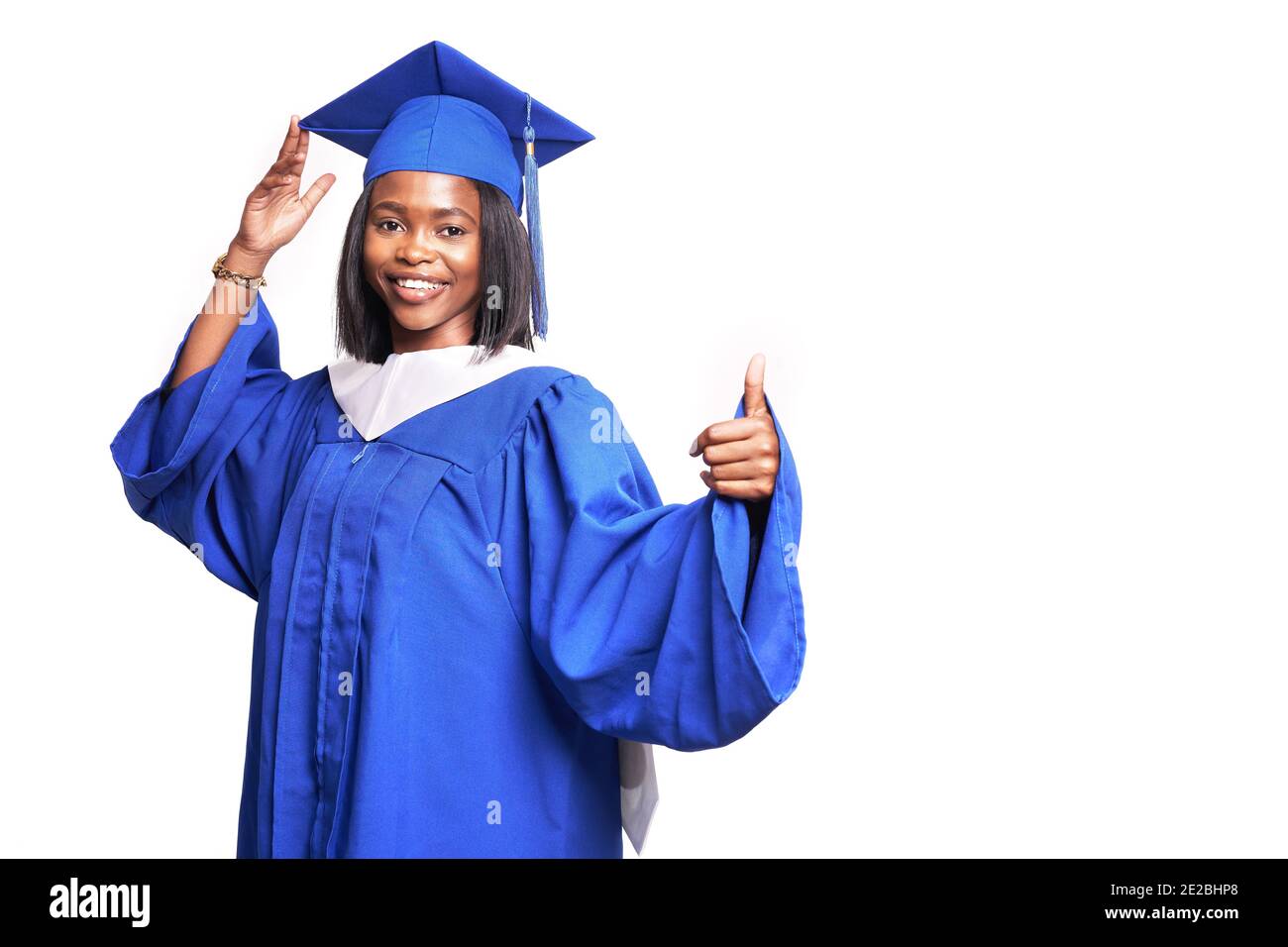 Afroamerikanische schöne Frau in einem blauen Gewand und Hut, auf einem weißen isolierten Hintergrund lächelt und zeigt Daumen nach oben Stockfoto