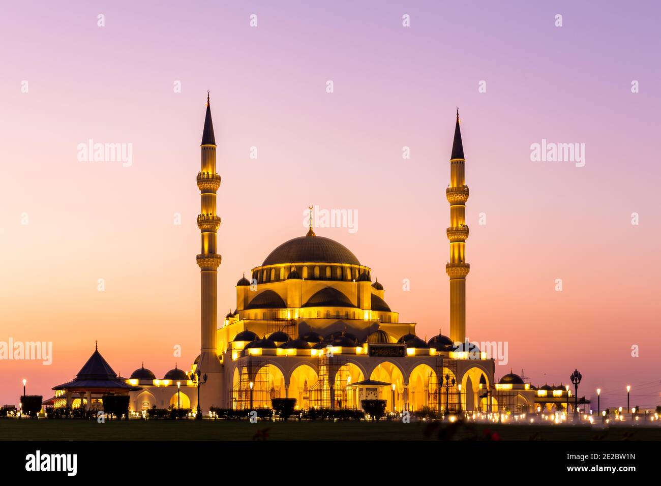 Neue Sharjah Moschee, die größte Moschee im Emirat Sharjah, die Vereinigten Arabischen Emirate, mit rosa Himmel Sonnenuntergang und Fassade Beleuchtung. Stockfoto