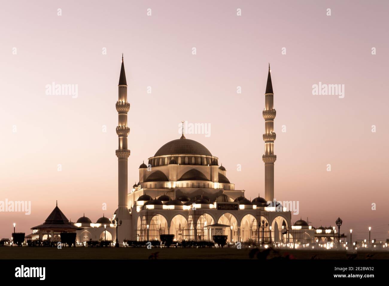 Neue Sharjah Moschee, die größte Moschee im Emirat Sharjah, die Vereinigten Arabischen Emirate, mit rosa Himmel Sonnenuntergang und Fassade Beleuchtung. Stockfoto