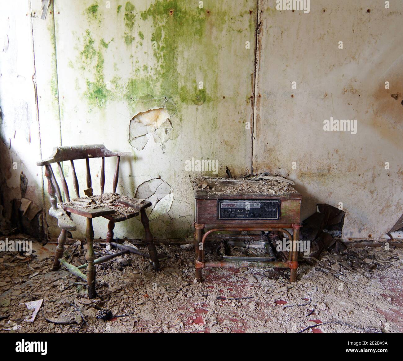 Verlassene Stelle - kaputter Stuhl und alter Radiokabinett Vorderseite einer moosigen Wand Stockfoto