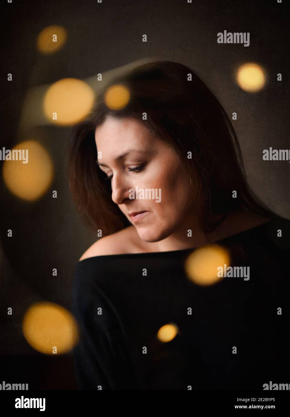 Nachdenkliche hübsche Frau in dunklem Zimmer mit hellem Bokeh Umgebung Sie Stockfoto