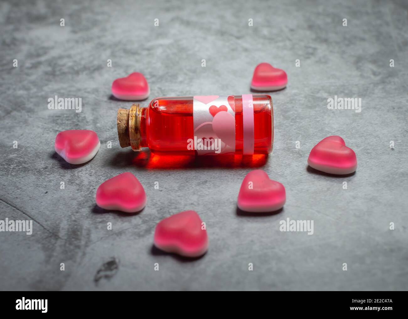 Nahaufnahme eines roten Liebestopfes in einem Glas Stopper Flasche umgeben von rosa herzförmigen Süßigkeiten liegend Eine strukturierte Oberfläche aus Beton Stockfoto