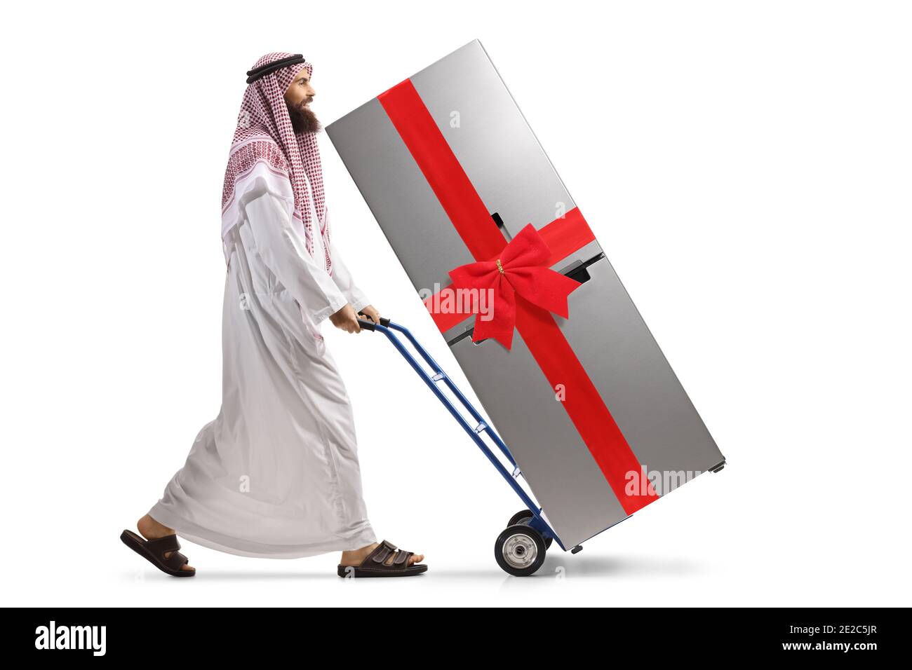 Ganzkörperaufnahme eines saudi-arabischen Mannes, der schiebt Ein Kühlschrank mit einem roten Bogen auf einem Handwagen isoliert Auf weißem Hintergrund Stockfoto