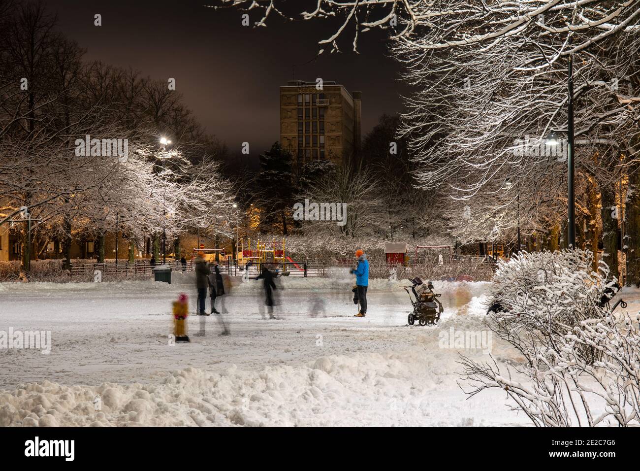 Bewegung verwischen Menschen im schneebedeckten Kirjailijanpuisto Park nach Einbruch der Dunkelheit mit Lastenlinna im Hintergrund im Taka-Töölön Bezirk von Helsinki, Finnland Stockfoto