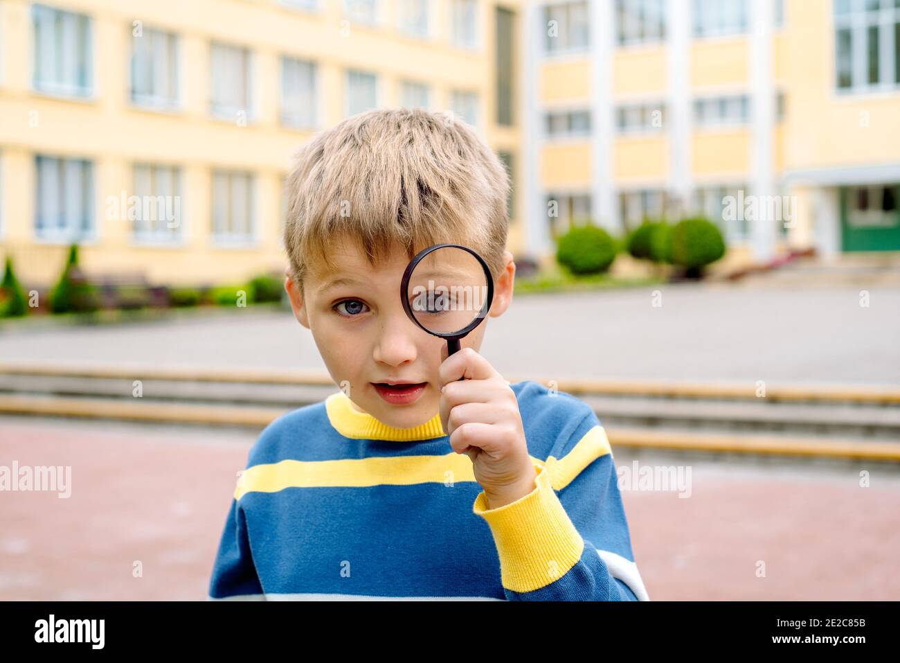 Neugierig überrascht Junge. Ein Schuljunge mit einer Lupe in der Nähe seines Auges im Schulhof. Junger Forscher, Ausbildung und Wissenschaft. Schulkonzept. Stockfoto