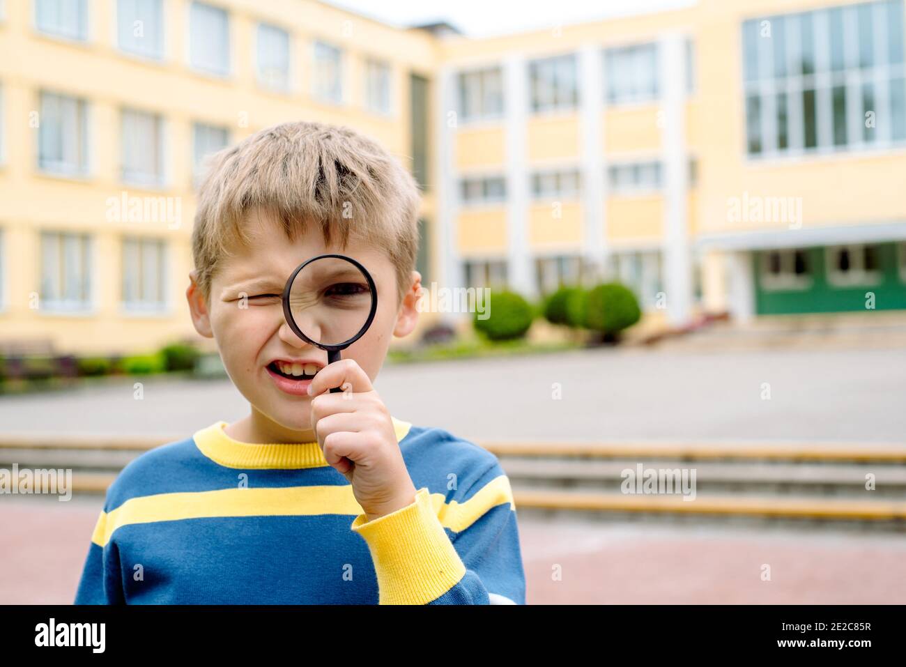 Neugierig überrascht Junge. Ein Schuljunge mit Lupe in der Nähe seines Auges im Schulhof. Junger Forscher, Ausbildung und Wissenschaft. Schulkonzept. Stockfoto