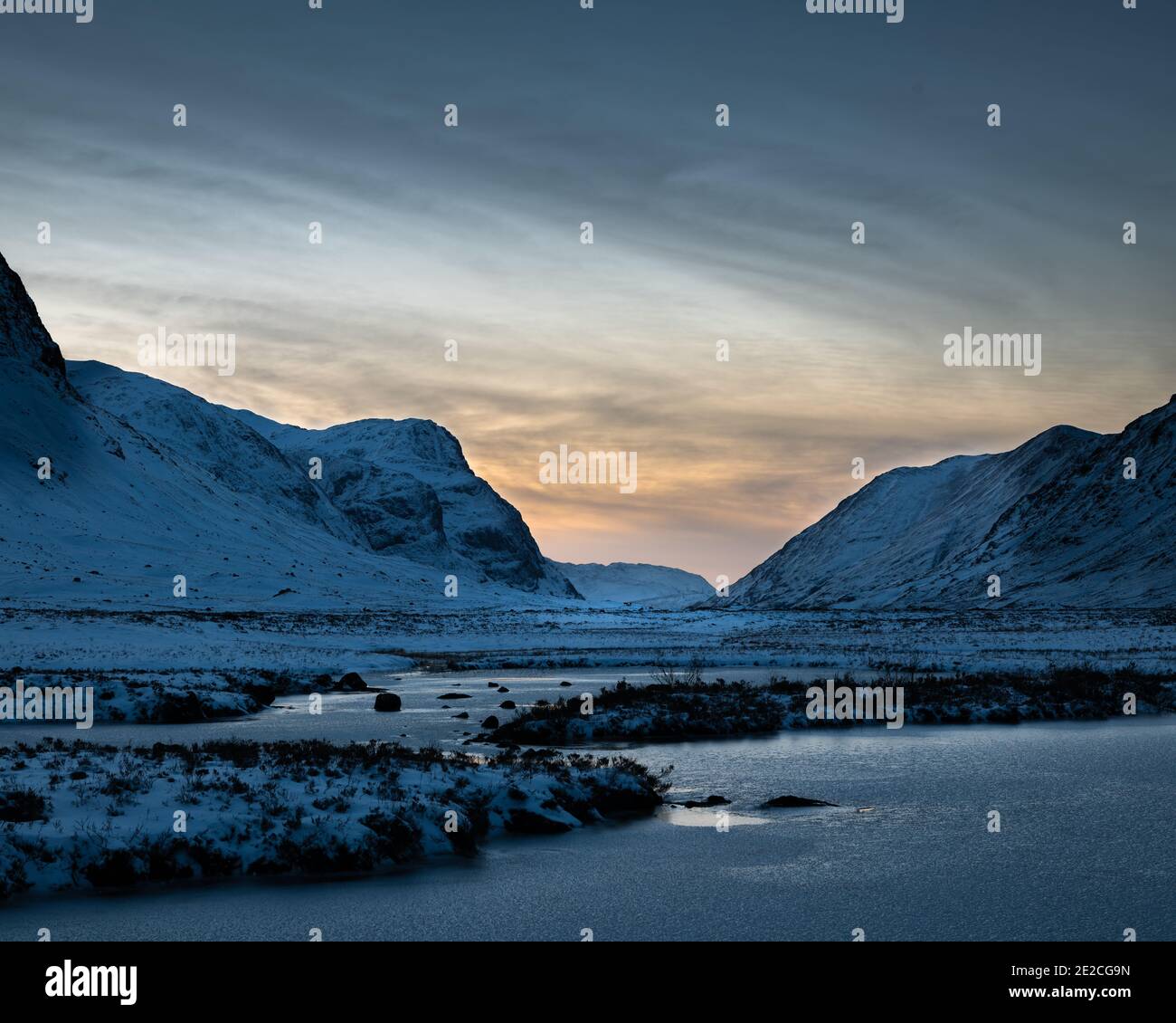 Blick nach Norden durch den Pass von Glencoe bei Sonnenuntergang an einem verschneiten Wintertag. Rotwild ernähren sich in der Ferne unterhalb der drei Schwestern von Glencoe. Stockfoto