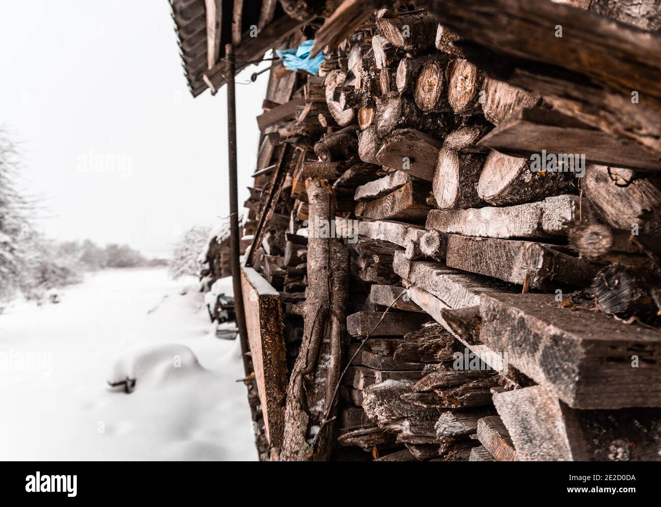 Brennholz und Bretter liegen in der Nähe der Hauswand Unter einem Dach und es gibt viel Schnee Draußen Stockfoto