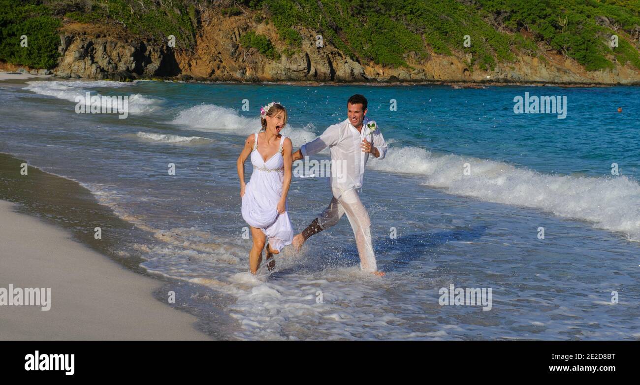 Das frisch verheiratete Paar feiert seine Hochzeit an einem Strand auf der karibischen Insel Mustique. Hand in Hand spritzen sie in die Brandung und schmeißen das Kleid ab. Stockfoto