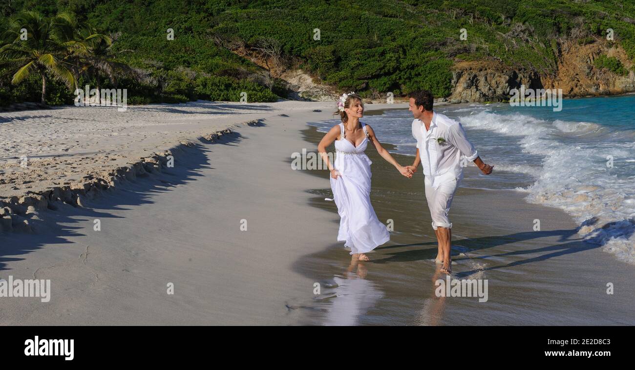 Das frisch verheiratete Paar feiert seine Hochzeit an einem Strand auf der karibischen Insel Mustique. Hand in Hand spritzen sie in die Brandung und schmeißen das Kleid ab. Stockfoto