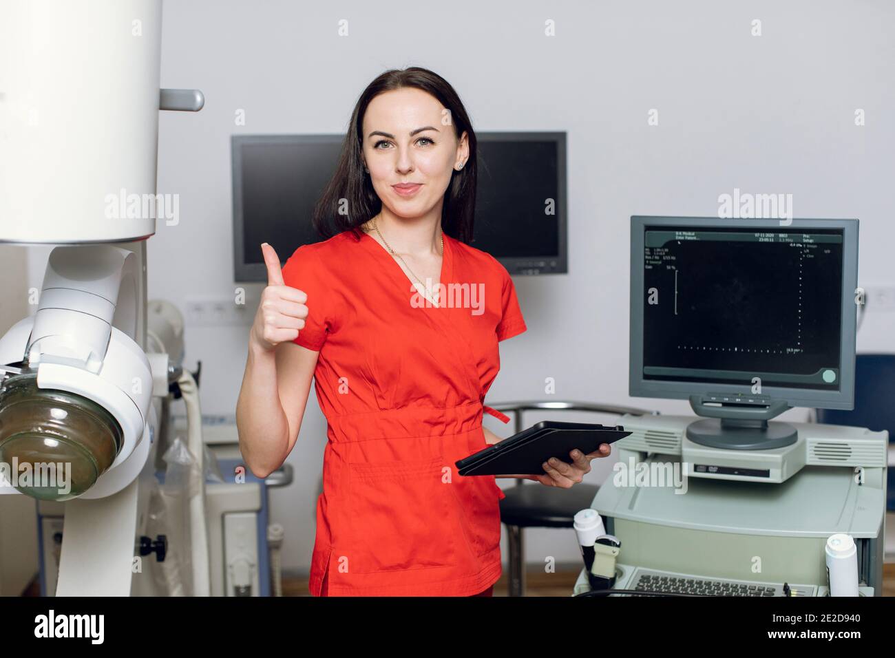 Nahaufnahme der hübschen kaukasischen Ärztin, die vor Ultraschall- und Lithotripter-Maschinen steht und den Daumen zeigt. Nicht invasiver Sicherheitsstein Stockfoto