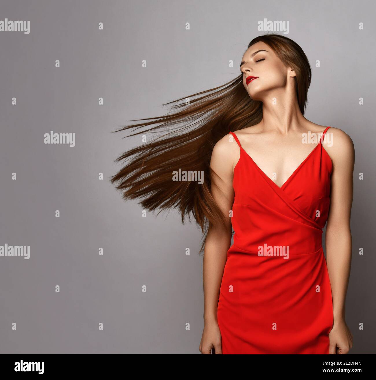 Junge Frau mit langen seidig geraden Haaren in rotem Kleid Steht schüttelnd Kopf macht ihre Haare fliegen auf Kopieplatz Stockfoto