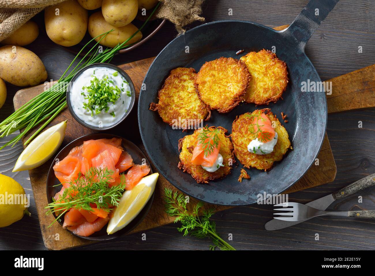 Knusprige Kartoffelpfannkuchen mit geräuchertem Lachs und Schnittlauch-Quark serviert In einer eisernen Pfanne Stockfoto