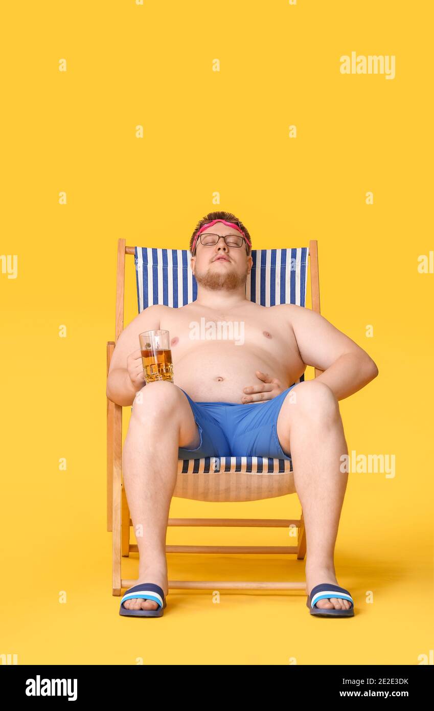 Übergewichtiger Mann mit einem Glas Bier, der vor farbigem Hintergrund auf  einem Strandstuhl sitzt. Gewichtsverlust Konzept Stockfotografie - Alamy