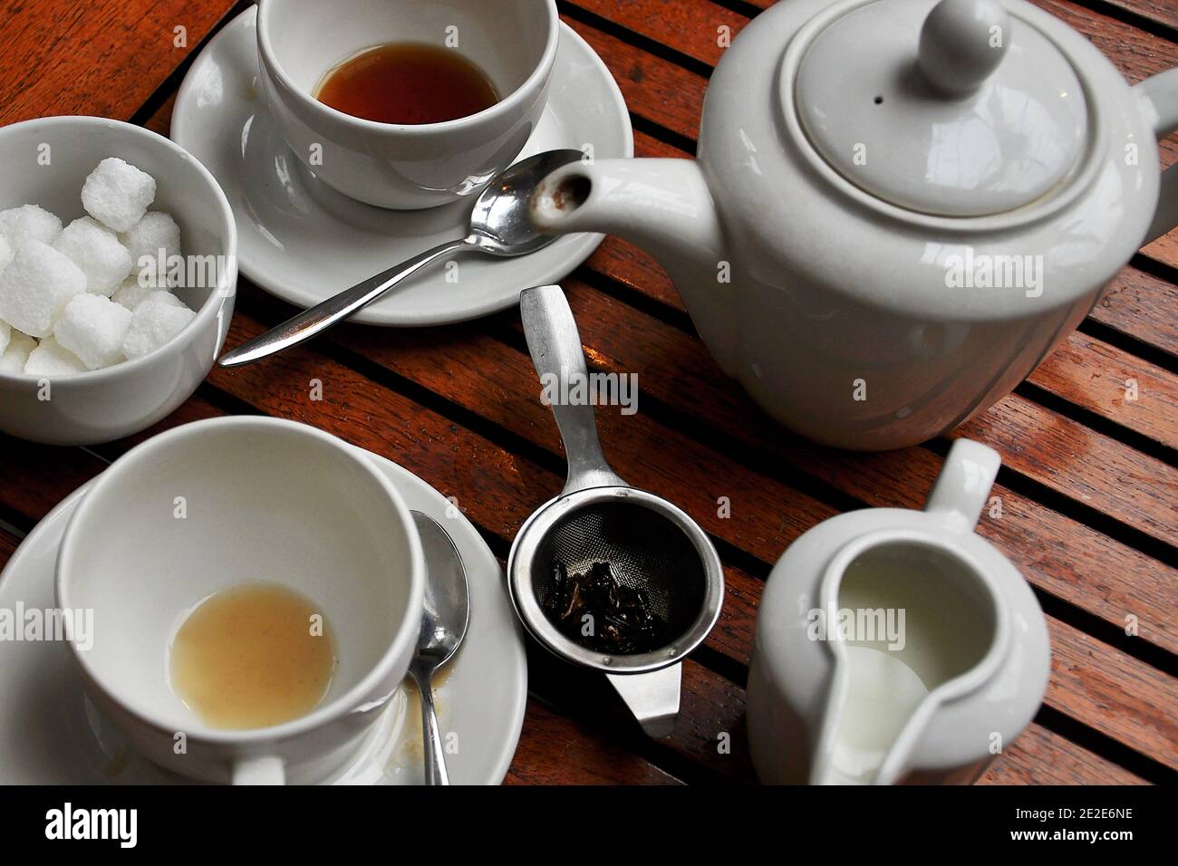 Überblick über einen abgeschlossenen Teeservice für zwei Personen mit leerten Teetassen, einer Teekanne, Zuckerwürfeln, Milchkanne und losem Teesieb auf dem Bistro-Tisch im Freien Stockfoto