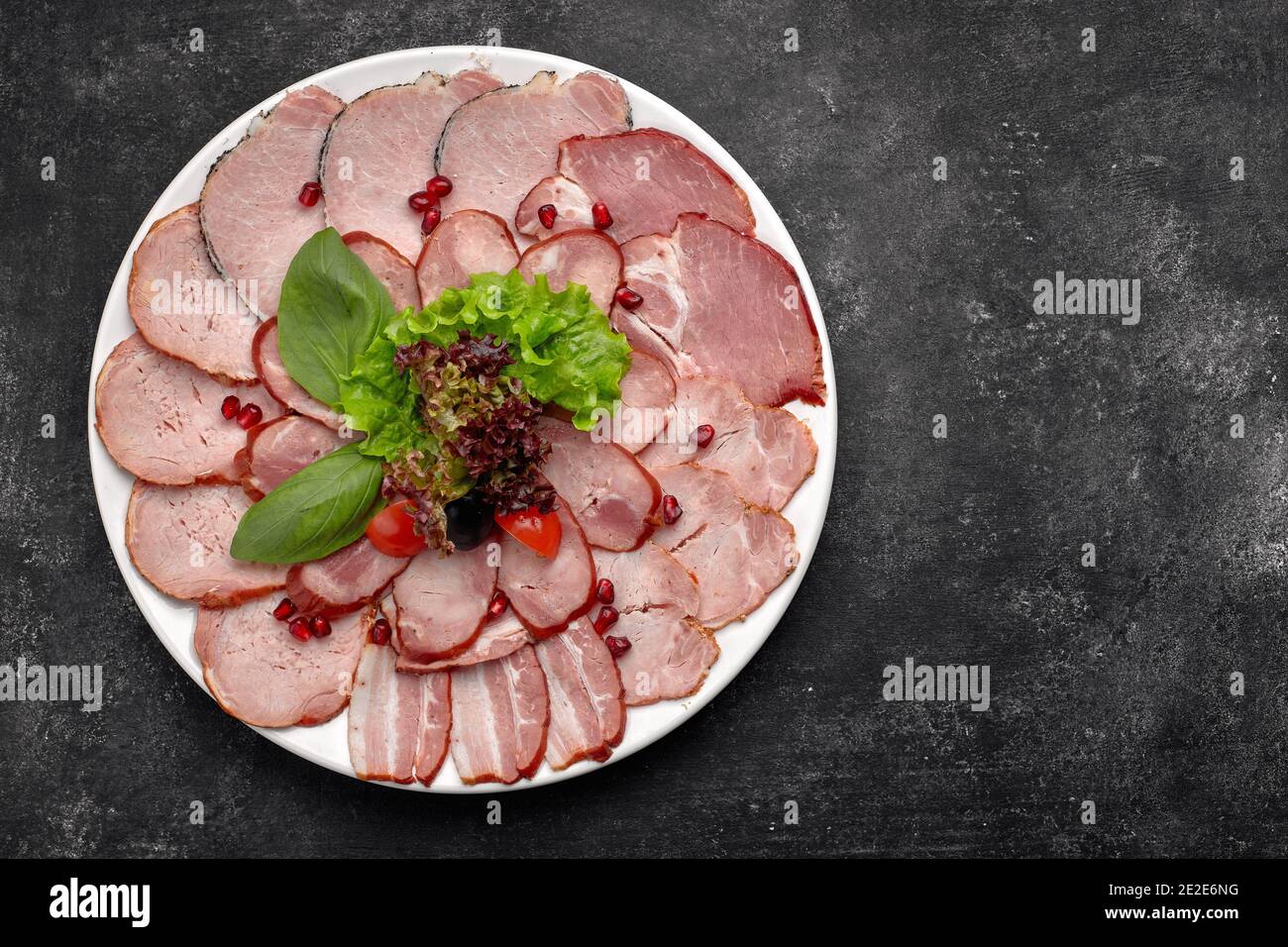 Aufschnitt in dünne Scheiben, Wurst, Speck, gekochtes Schweinefleisch,  Fleisch, mit Salat, Basilikum, Kirschtomaten und Granatapfelkernen, auf  einem weißen Teller Stockfotografie - Alamy