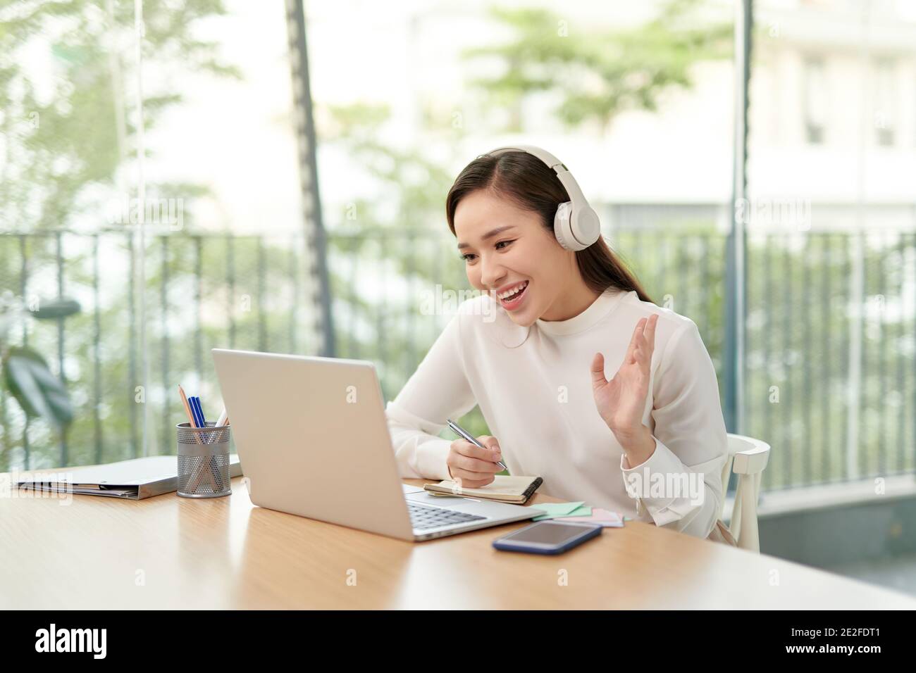 Süßes Mädchen, das am Laptop mit einem Headset auf dem Kopf arbeitet. Spaß haben und über das Internet surfen. Stockfoto