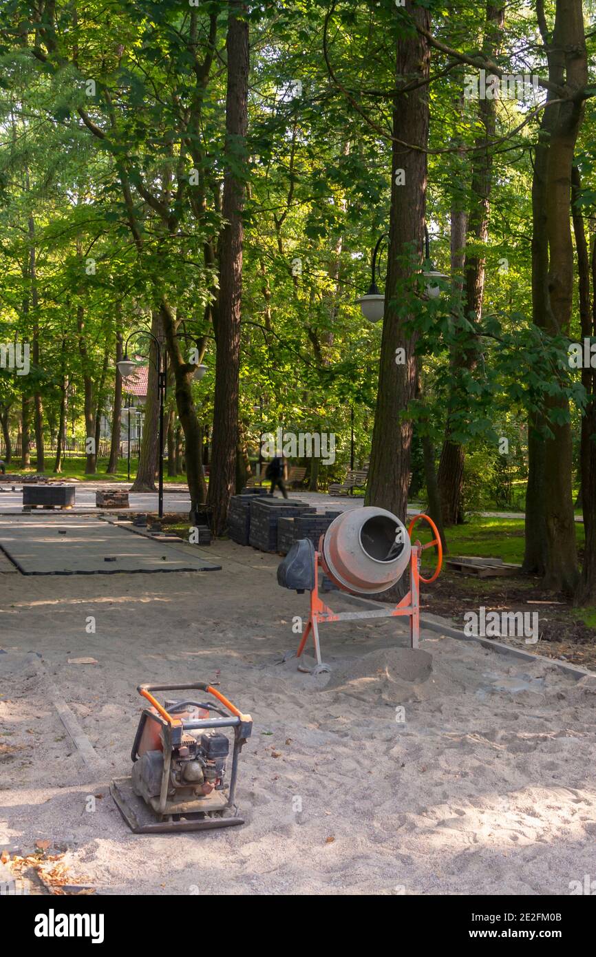 Bauarbeiten im Stadtpark. Betonmischer und Vibrationsplatte für die Reparatur von Pflasterplatten zum Sand. Selektiver Fokus. Stockfoto