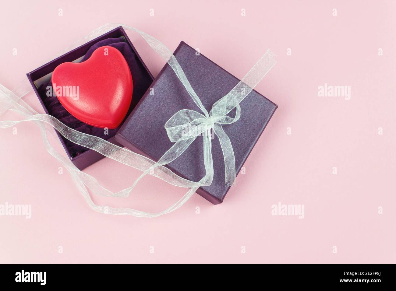 Geschenkbox in lila Farbe mit rotem Herz auf einem rosa Hintergrund. Valentine-Konzept Stockfoto