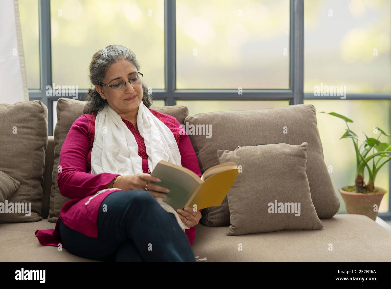EINE ÄLTERE ERWACHSENE FRAU, DIE SITZT UND BUCH LIEST Stockfoto
