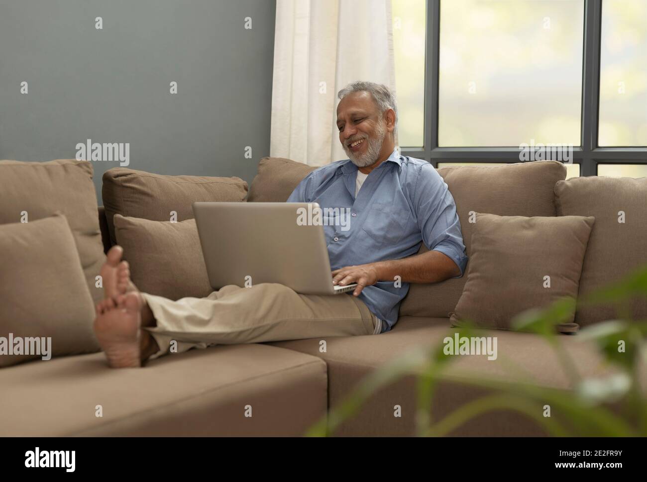 EIN ÄLTERER ERWACHSENER SITZT GLÜCKLICH UND BENUTZT LAPTOP Stockfoto