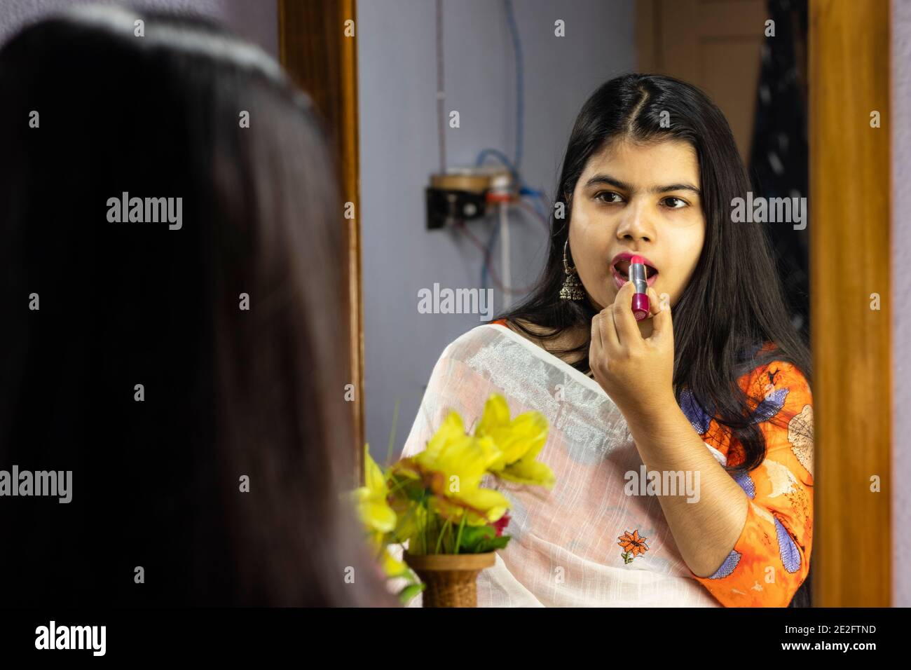 Eine schöne indische Frau in weißem Saree Anwendung Lippenstift in Vorderseite des Spiegels mit lächelndem Gesicht Stockfoto