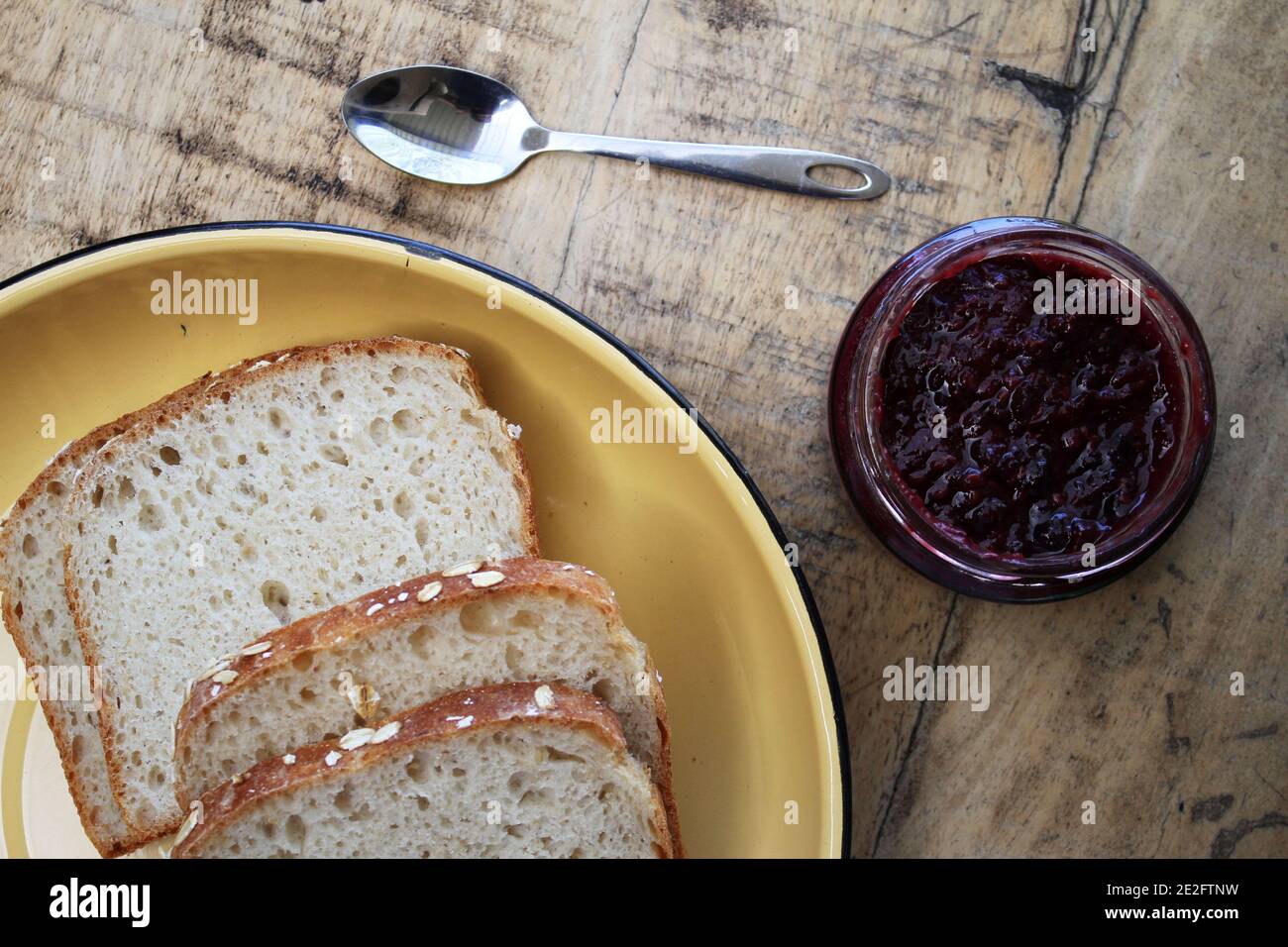 Eine Marmelade aus Glas neben einem Teller Brot Und einen Löffel vor einer rustikalen Holzkulisse Stockfoto