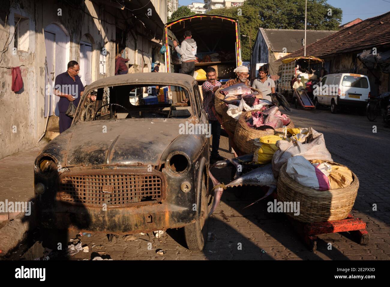 Vor dem Fischerhafen Sassoon Docks in Colaba, Mumbai, Indien, und neben einem kaputten alten Auto laden Träger zerschnittener Segelfische auf einen Lastwagen Stockfoto