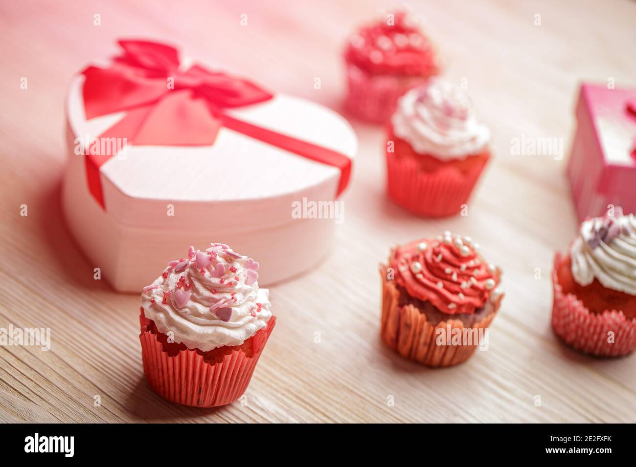 Valentinstag Komposition. Cupcakes mit Schlagsahne und herzförmigen Streuseln, herzförmige Geschenkbox Stockfoto
