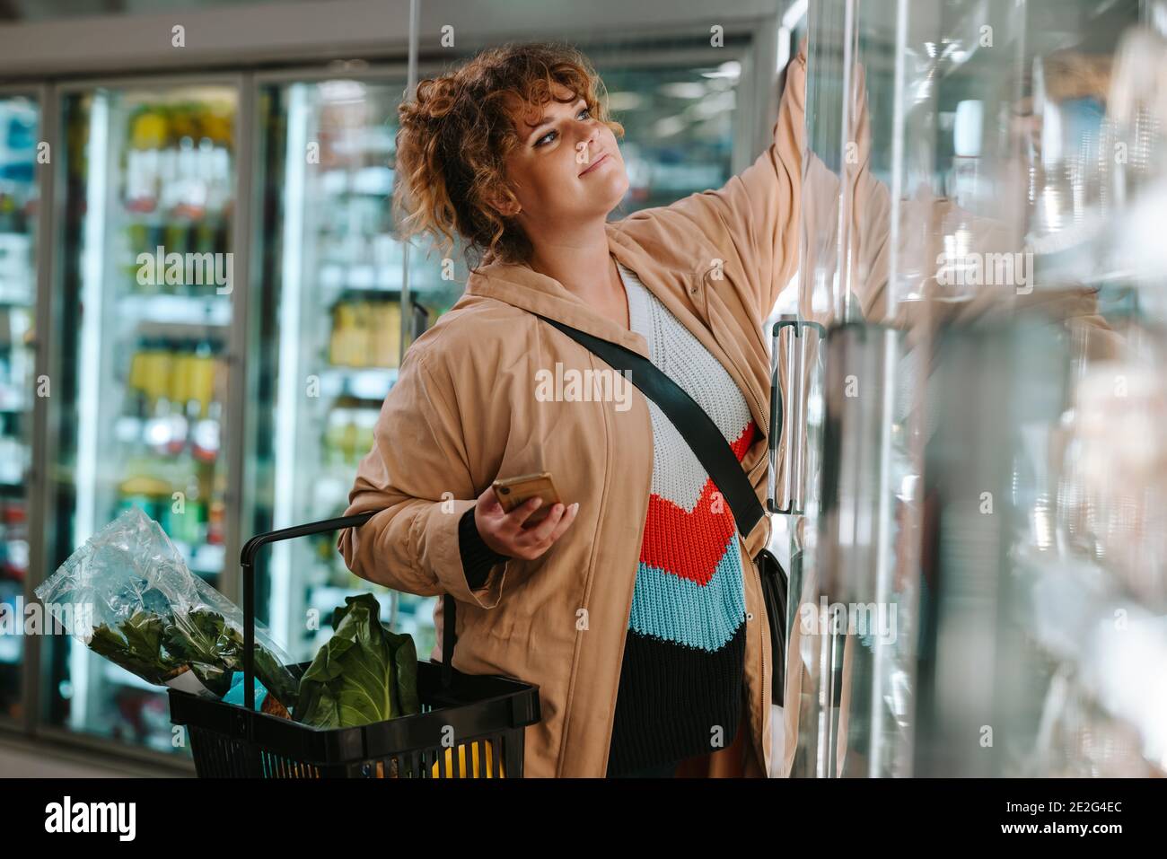 Weibliche Shopper erreichen Produkt aus dem Gefrierschrank im Supermarkt. Frau, die Lebensmittel aus einem Lebensmittelgeschäft kauft. Stockfoto
