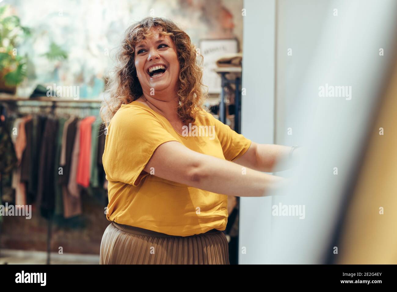 Eine Kundin lächelt, während sie die Kleidung auf dem Regal im Geschäft ansieht. Weibliche Shopper im Bekleidungsgeschäft. Stockfoto