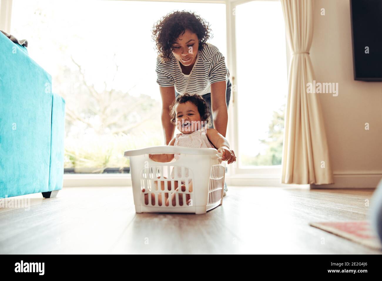 Frau schob lächelndes Baby, das im Waschkorb sitzt. Baby genießen Wäschekorb Fahrt zu Hause. Stockfoto