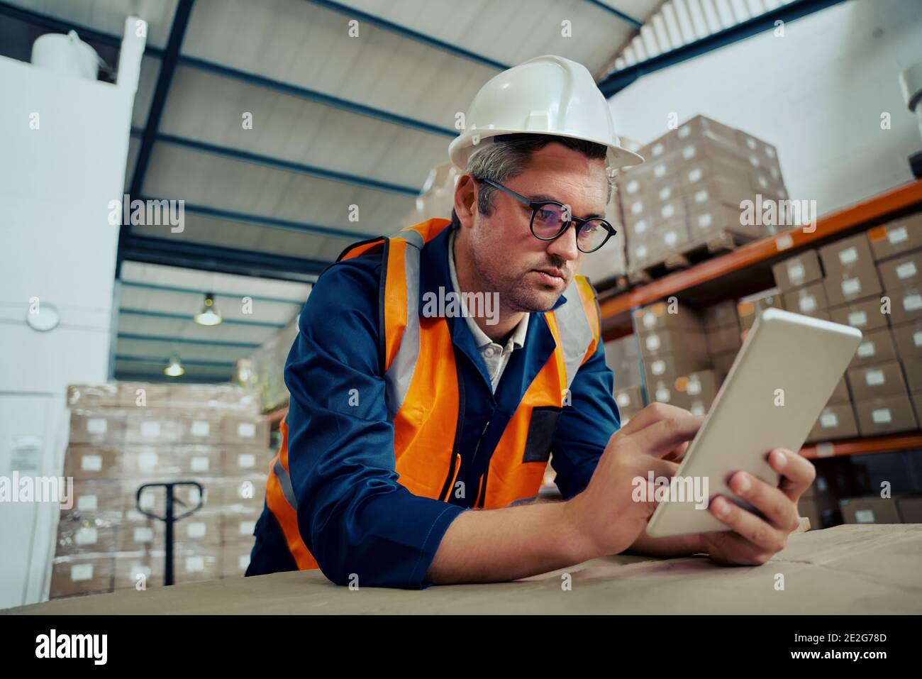 Männlicher Fabrikingenieur, der eine Brille mit einem digitalen Tablet trägt, auf das er sich stützt Tabelle Stockfoto