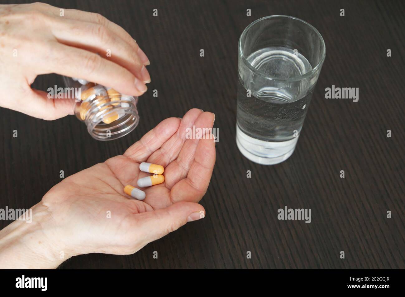 Frau mit Pillen in den Händen. Medikamente in Kapseln und Glas Wasser auf einem Tisch Stockfoto