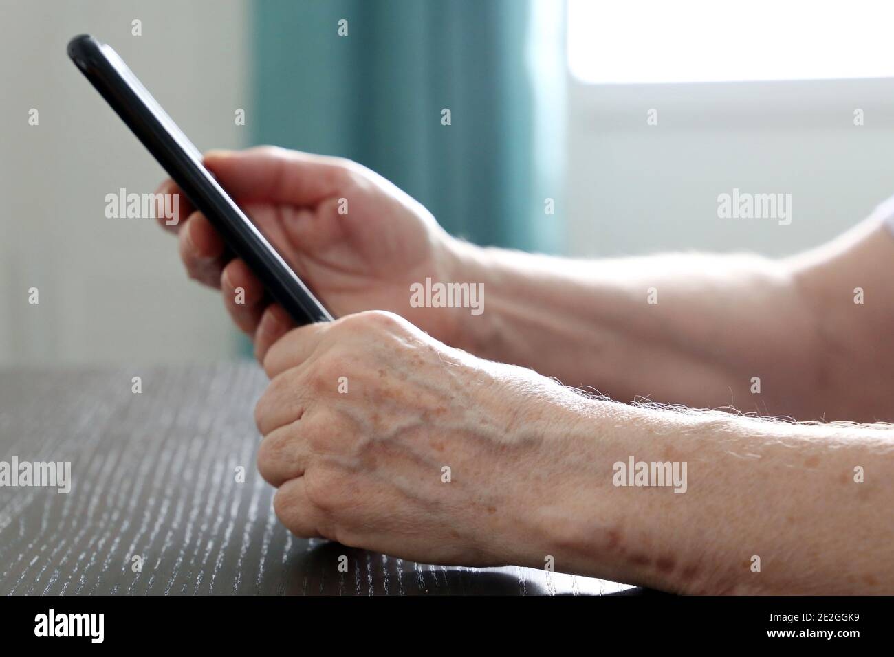 Ältere Frau mit Smartphone am Tisch sitzend, Handy in faltigen weiblichen Händen. Konzept der Online-Kommunikation im Ruhestand Stockfoto
