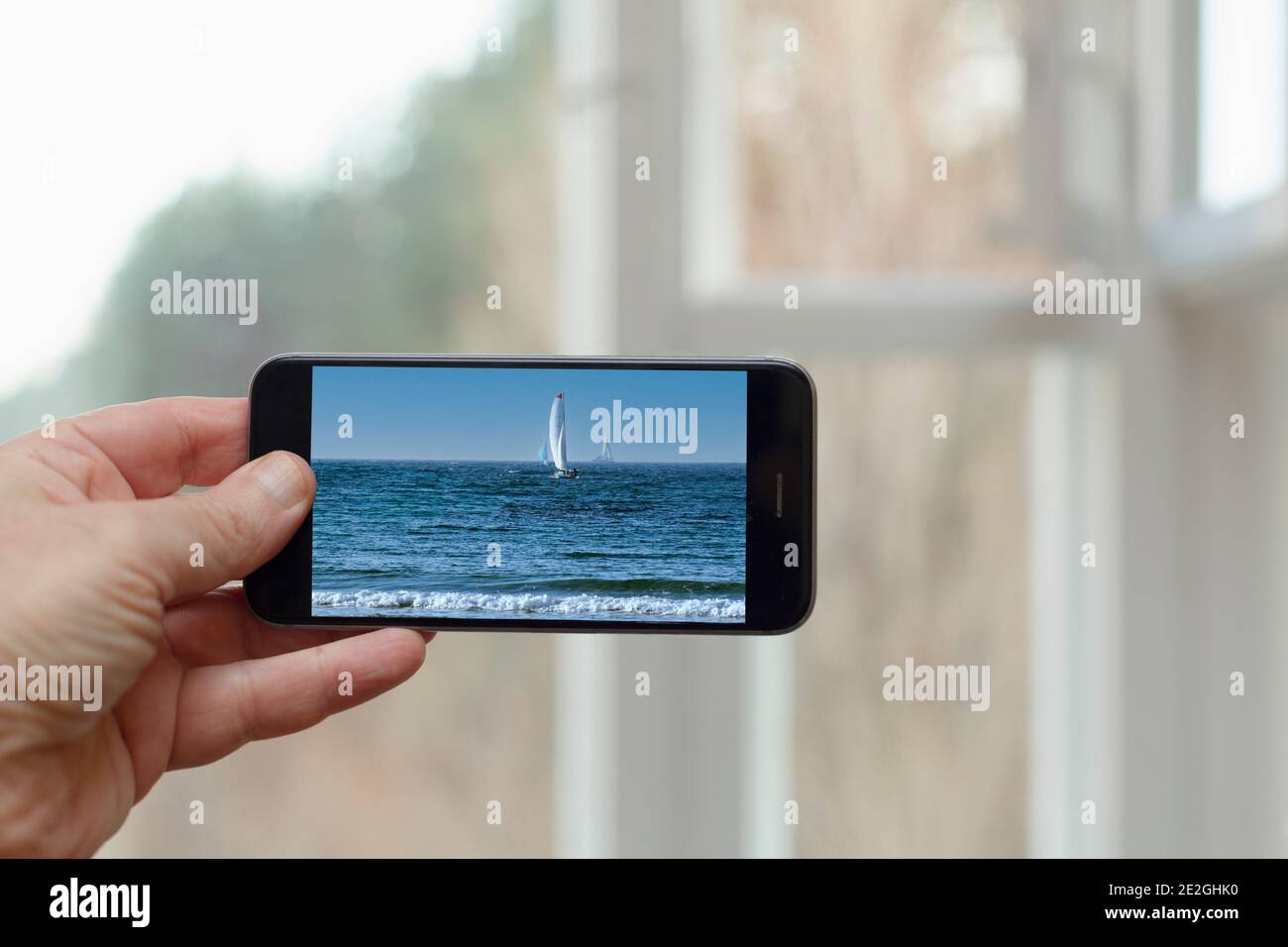 POV Person auf Foto von Segelboot und Meer auf Smartphone-Bildschirm Stockfoto