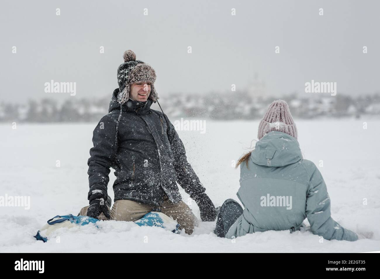 Mann mit Freundin, die in die Schneeröhre fällt. Junge glückliches Paar zu Fuß im Wintertag Stockfoto