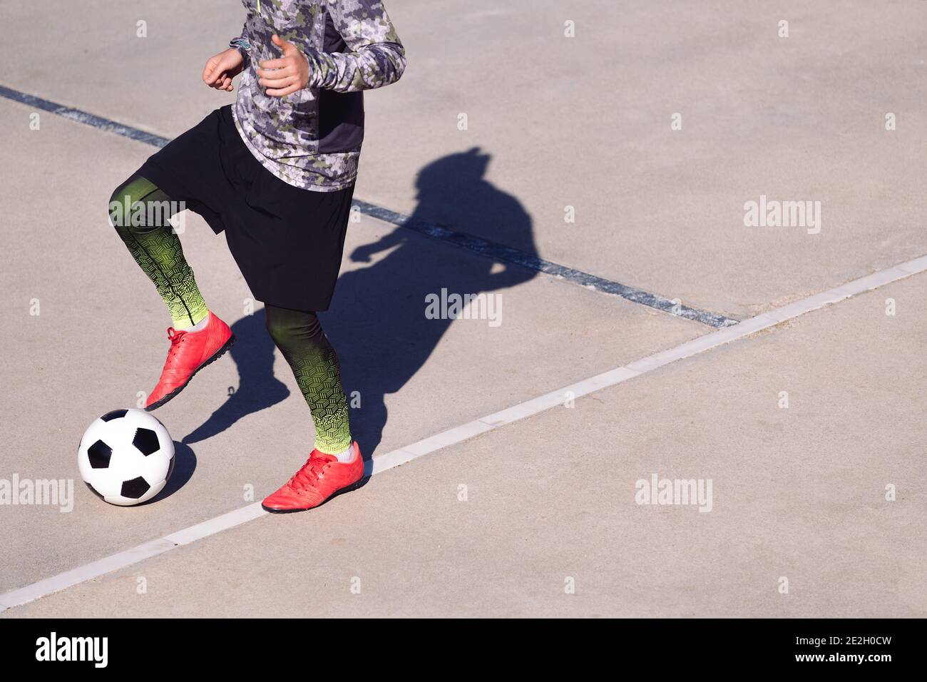 Beine eines nicht erkennbaren Fußballspielers, der den Ball auf einem Betonfußballplatz spielt, Konzept des gesunden Lebensstils und des städtischen Sports in der Stadt, Kopie Stockfoto