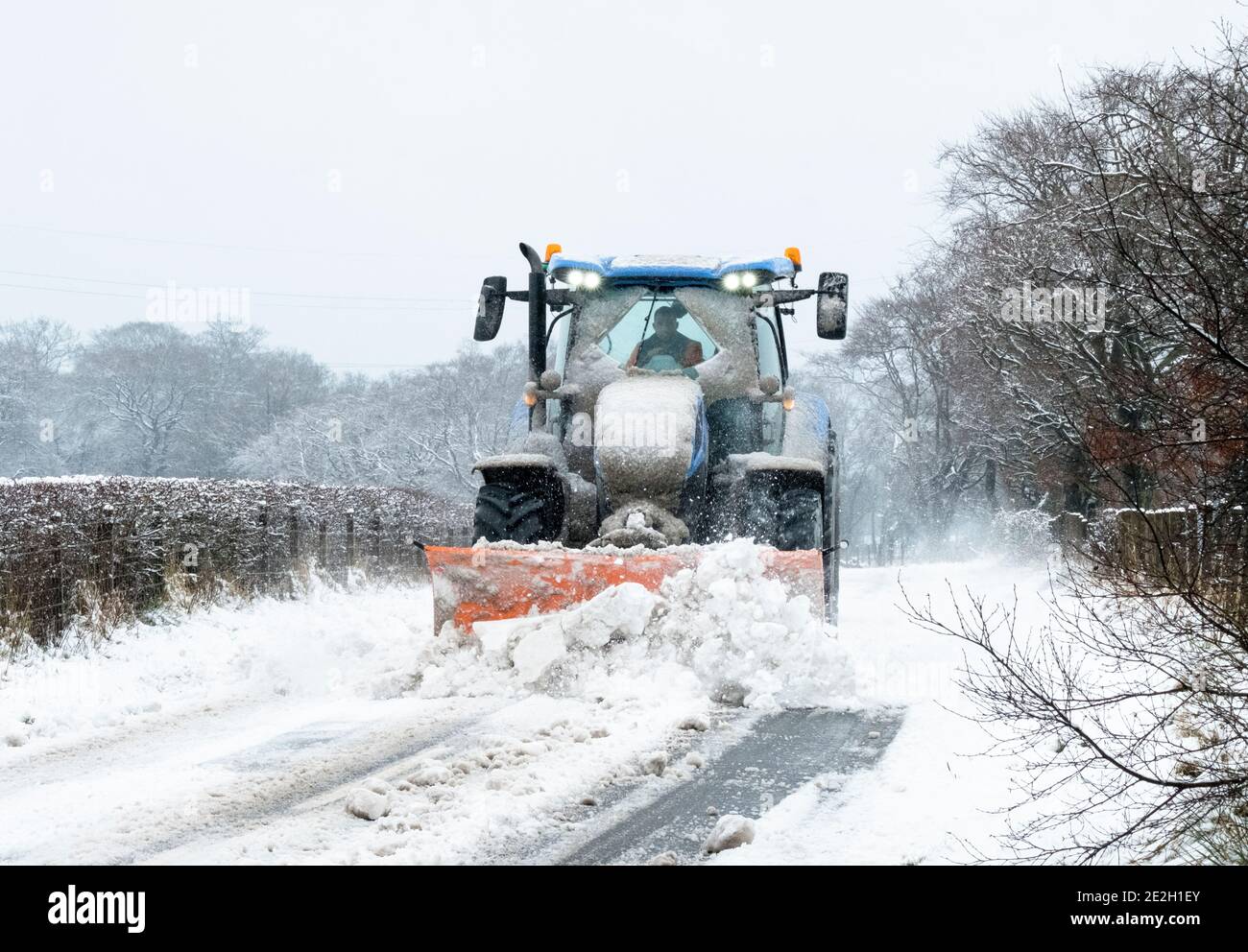 West Lothian, Schottland, Großbritannien. Wetter, 14. Januar 2021. Ein Traktor mit Schneepflug räumt nach nächtlichterndem Schnee eine Hinterstraße frei. West Calder, West Lothian, Schottland, Großbritannien. Quelle: Ian Rutherford/Alamy Live News. Stockfoto