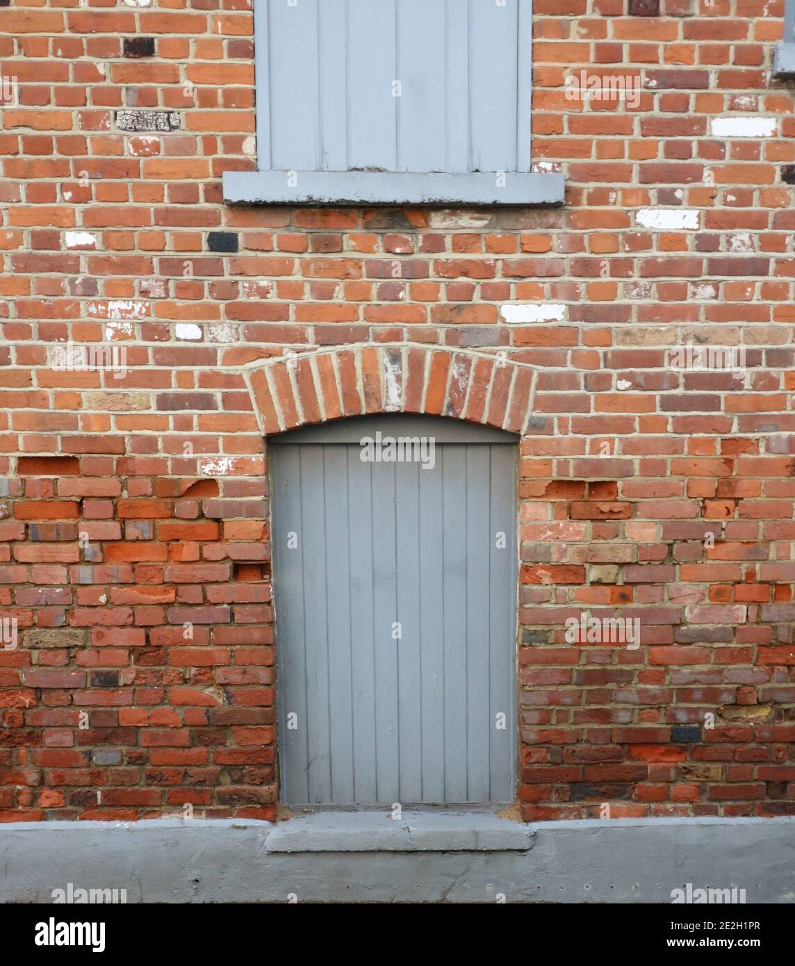 Sehr alte Backsteinmauer mit grauer Holztür und grau Blenden Stockfoto