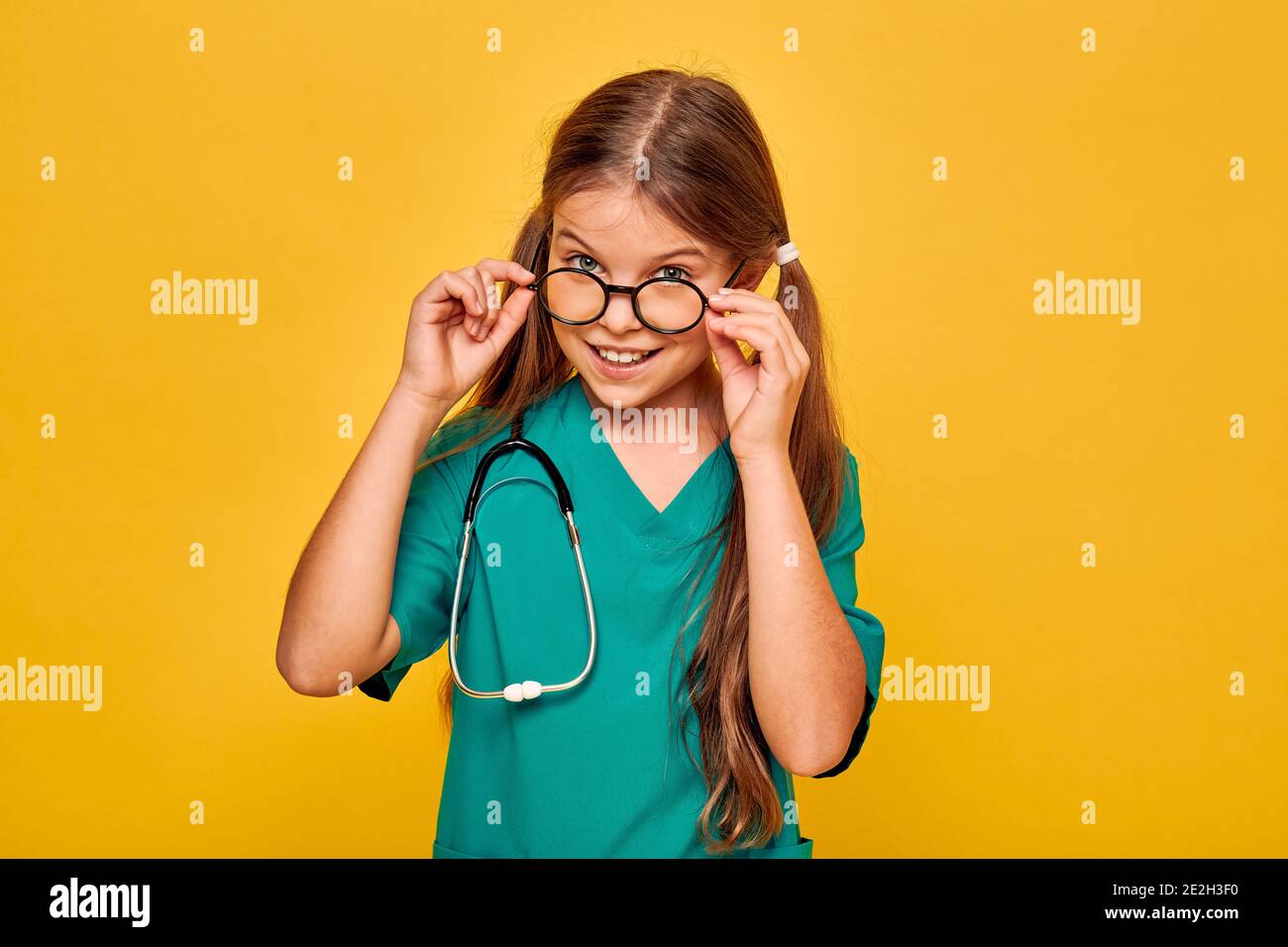 Mädchen trägt eine chirurgische Uniform und ein Stethoskop spielt den medizinischen Beruf, und zeigt auf ihrem Gesicht Emotion der Überraschung, Ausziehen der Brille, auf Ye Stockfoto