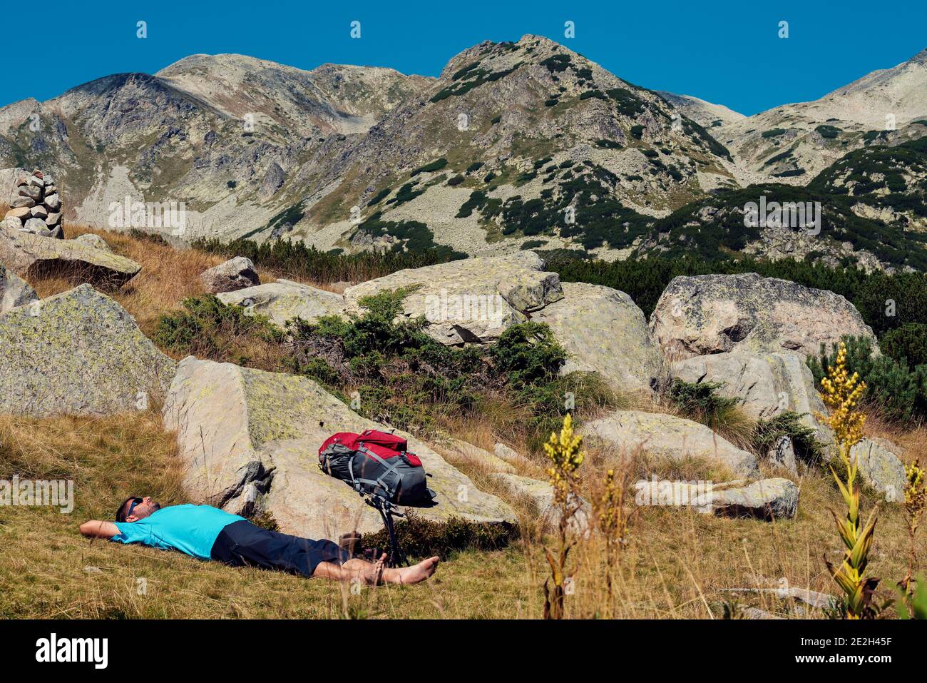 Kaukasischer Mann, der sich auf den Boden legt und sich entspannt Pirin Nationalpark Er hat seine Schuhe und Socken genommen Aus und haben seinen roten Rucksack auf ein h gelegt Stockfoto