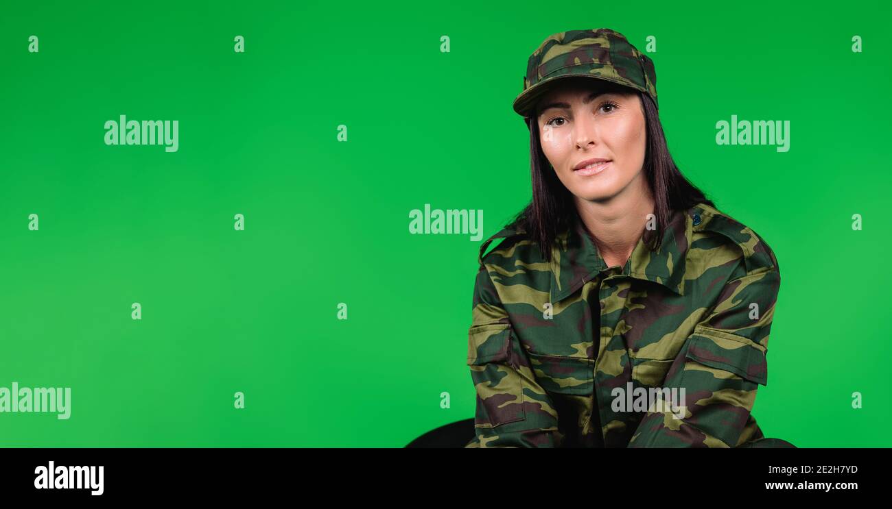 Banner – Langformat. Porträt einer niedlichen Frau in Militäruniform Blick in die Kamera auf einem grünen Hintergrund mit leeren Seitenraum. Stockfoto