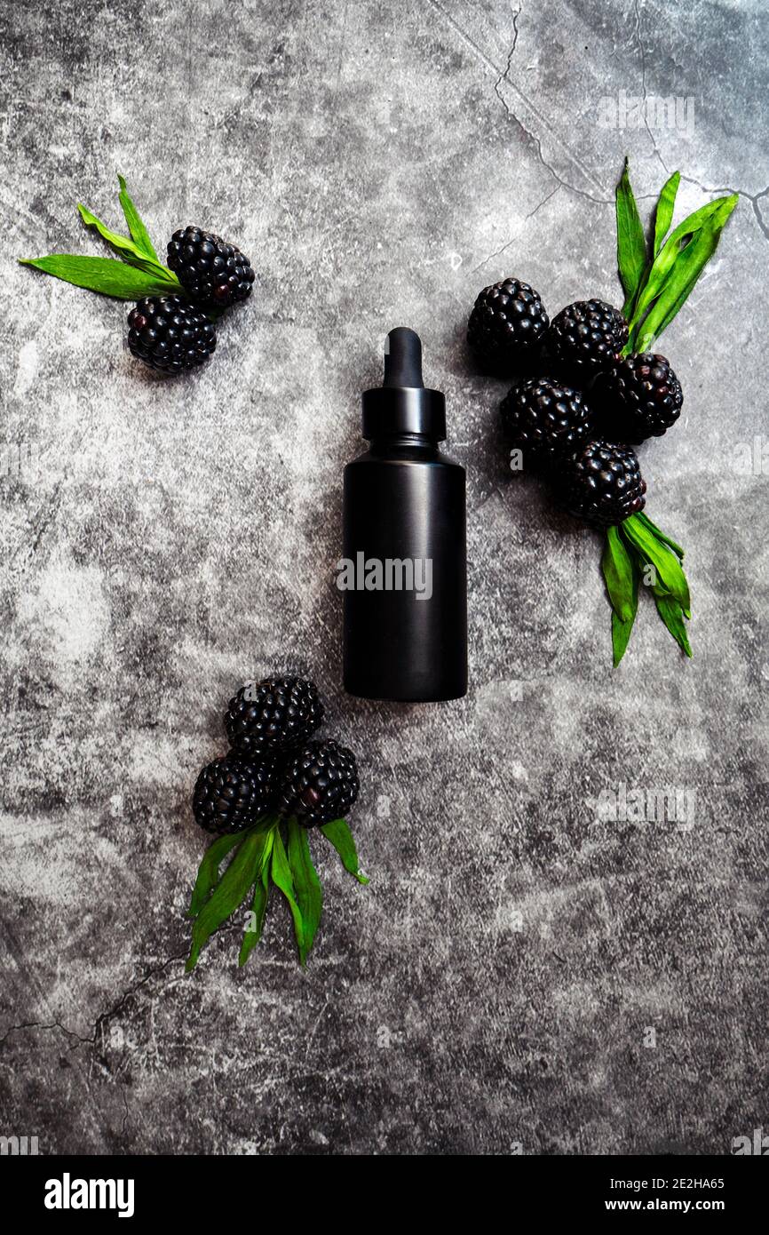 Schwarze Flasche Anti-Aging-Serum für Männer auf dunklem Hintergrund, umgeben von Brombeeren, die reich an Antioxidantien sind. Stockfoto