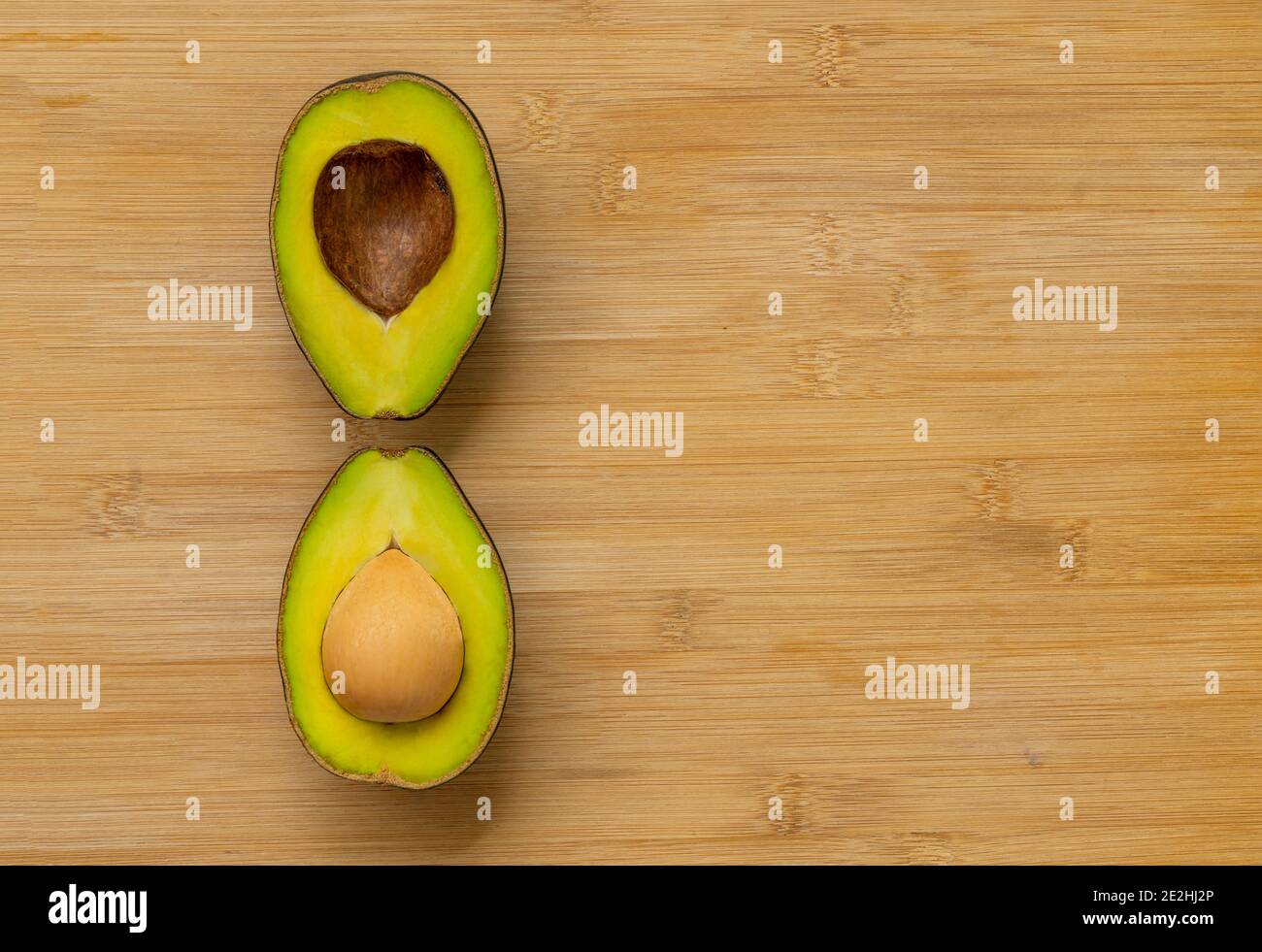 Zweischneidende halbe Avocados mit einzigartiger Anordnung auf Bambus-Schneidebrett, Draufsicht Bild, Platz für Kopie und Design. Stockfoto