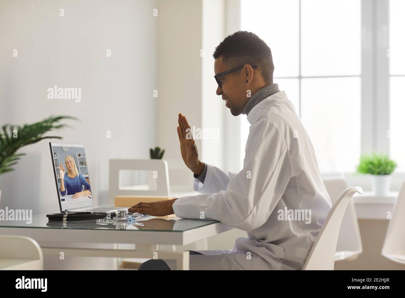 Arzt-Video ruft ältere Frau an und winkt Hand auf Laptop-Bildschirm und begrüßt sie Stockfoto