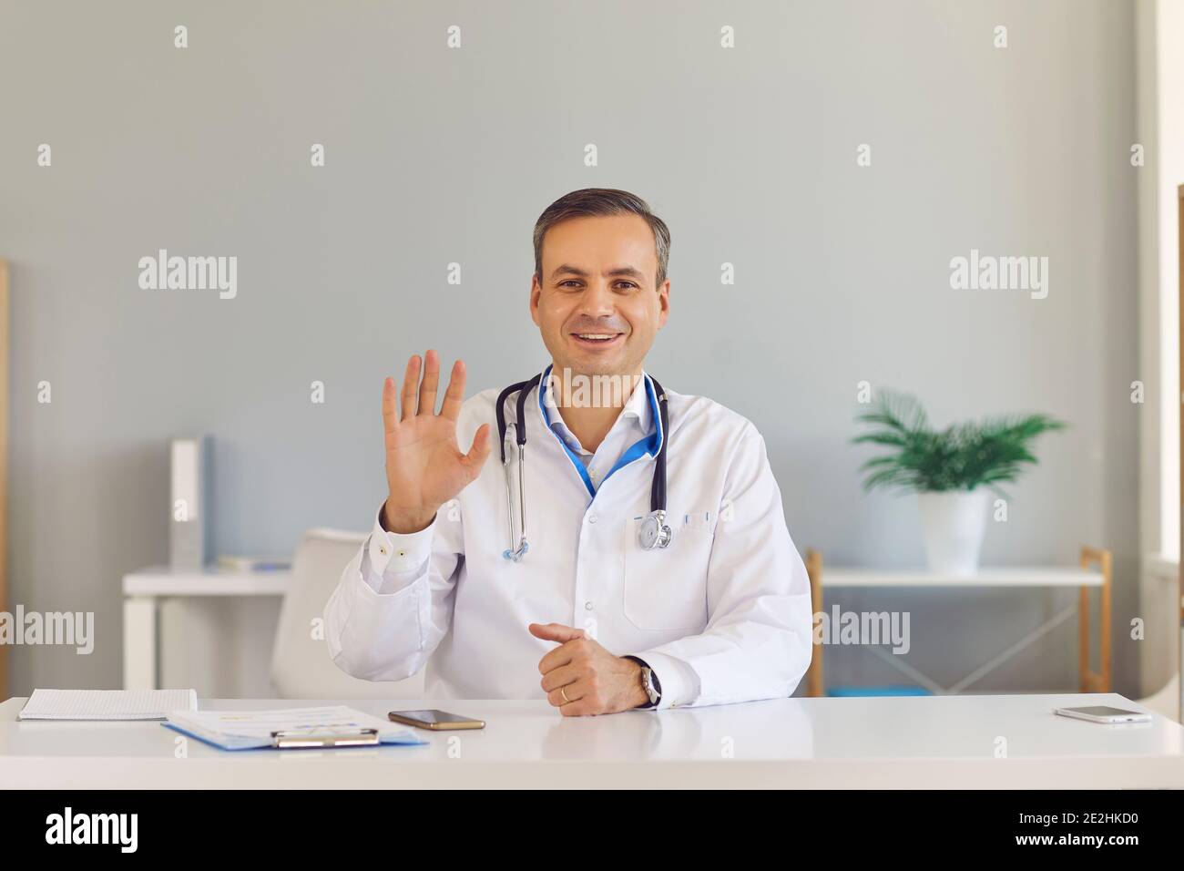 Freundlicher männlicher Arzt winkt seine Hand in Gruß geben eine Online-Beratung zu einem Patienten. Stockfoto
