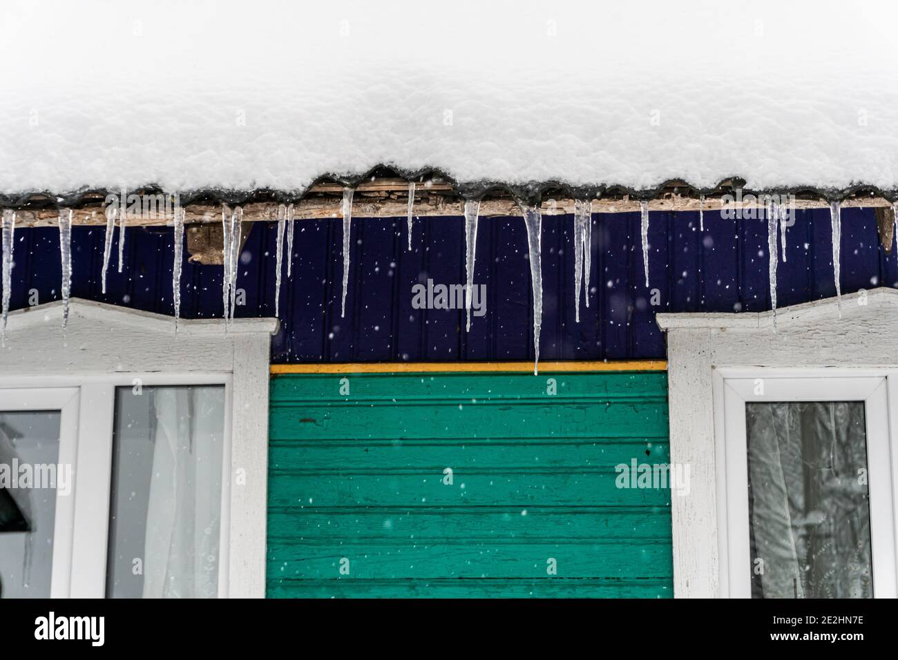 Im Winter hängen fallende Eiszapfen auf dem Haus, das Dach ist mit Schnee bedeckt, im Winter im Dorf Stockfoto