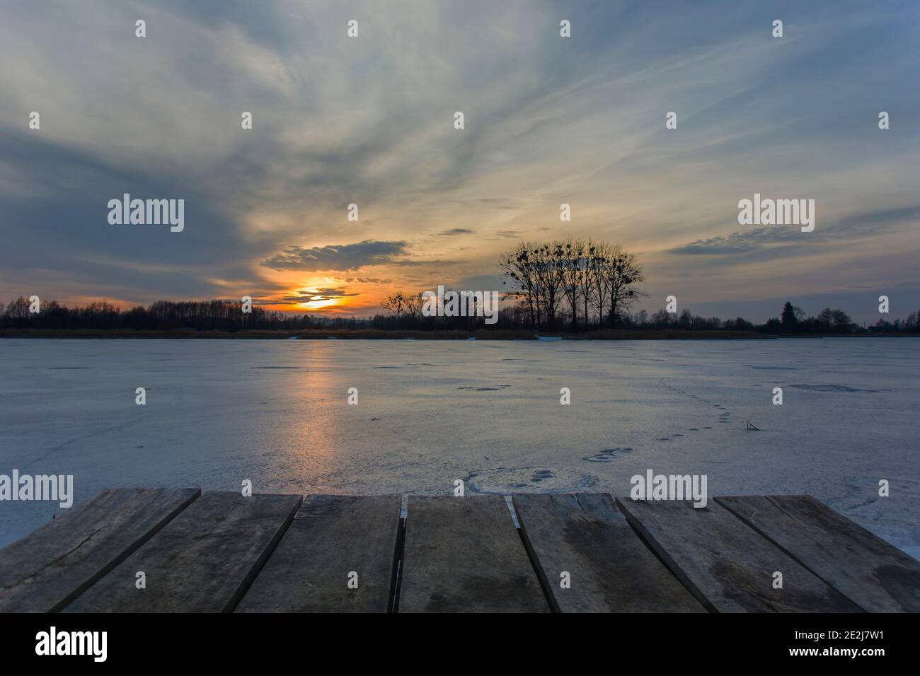 Plattform von Brettern auf einem gefrorenen See, schöner Sonnenuntergang am Himmel, Winterblick Stockfoto